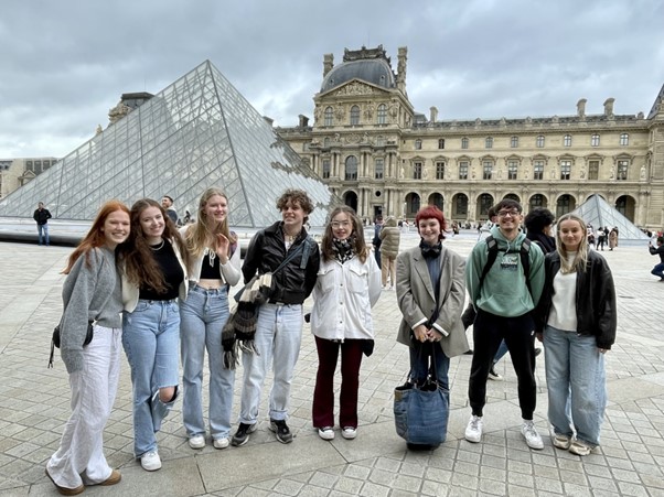 a group of students standing in front of the glass pyramid at the Louvre